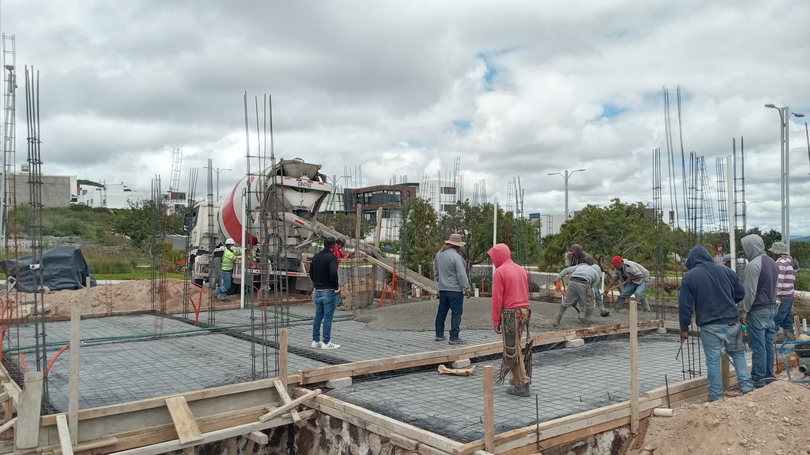 Colado de la losa de cimentación de una residencia en Zibatá: camión revolvedor descargando por canalón mientras la cuadrilla extiende y regletea el concreto entre las jaulas de armado de las columnas.