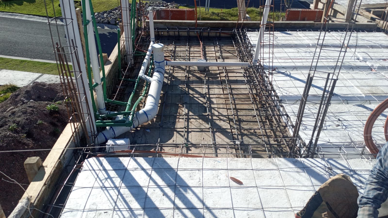 Instalación hidrosanitaria antes del colado: tubería hidráulica verde de PPR y bajadas sanitarias de PVC ruteadas contra el muro y a través de la losa armada.