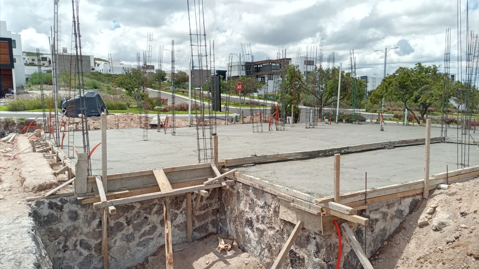 Cimentación terminada de la residencia: plataforma de concreto colada con arranques de columna y muros de contención de mampostería de piedra bajo el nivel de calle.