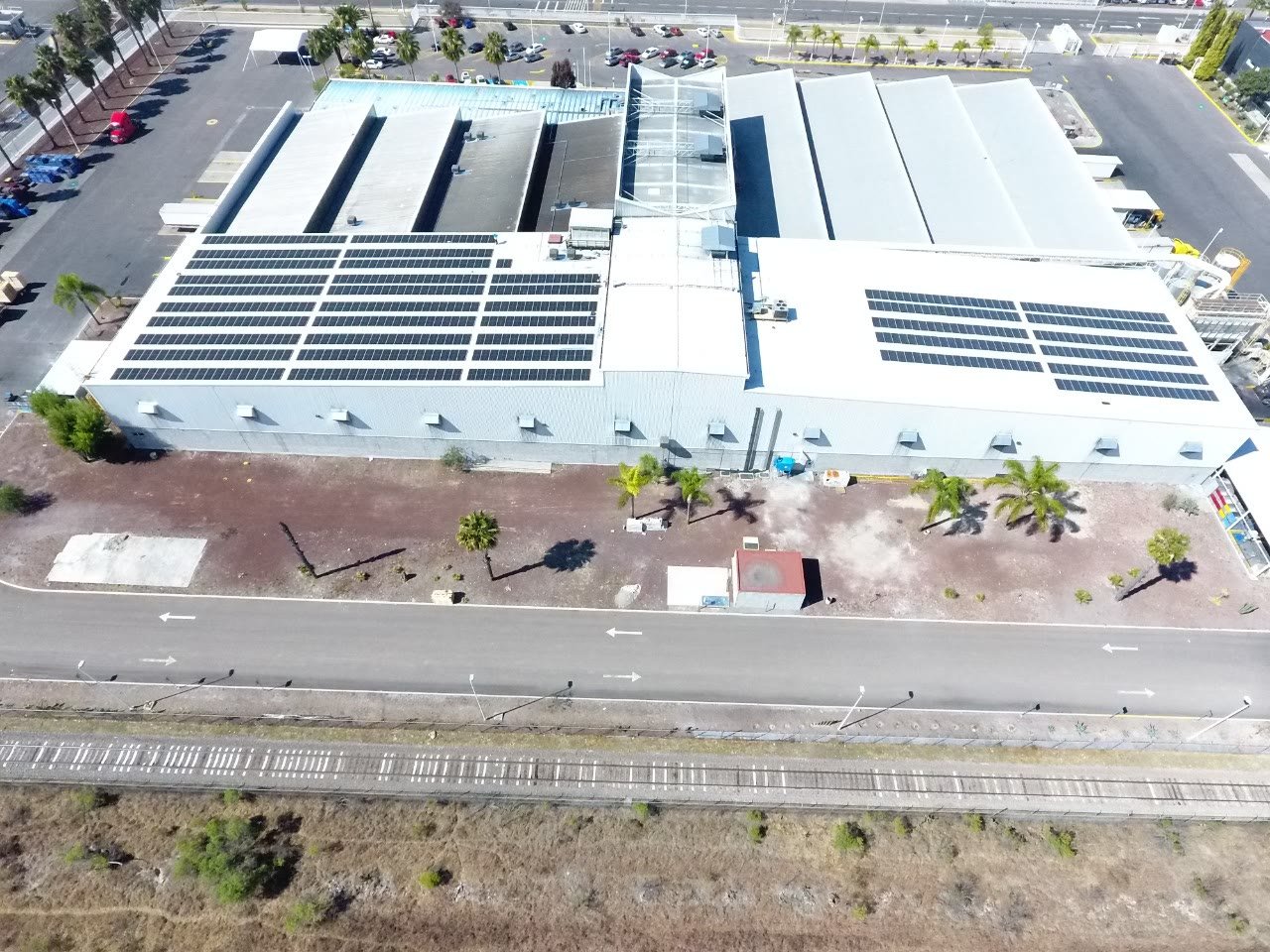 Vista aérea de una nave industrial en Querétaro con cubiertas a dos aguas y campos de paneles solares sobre azotea