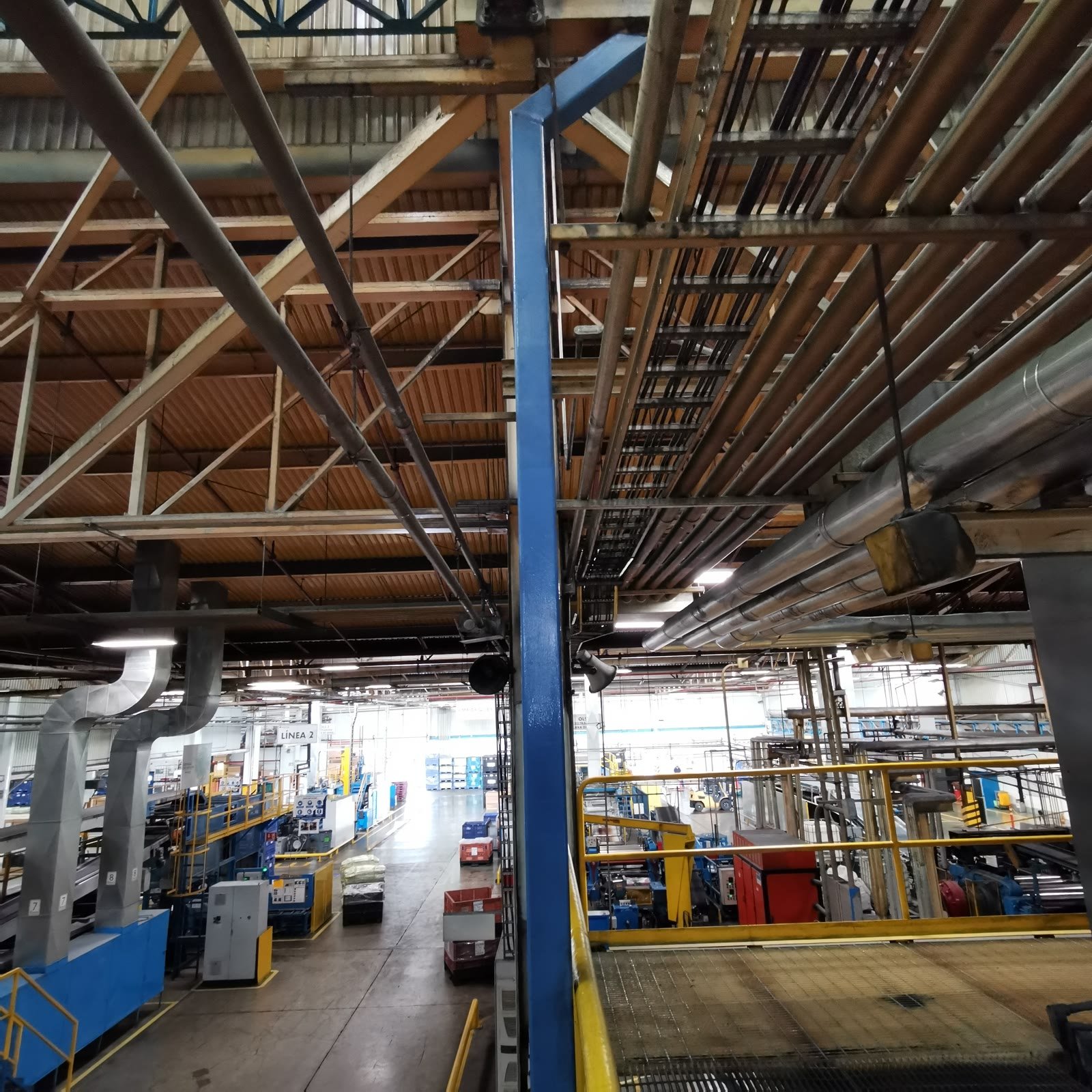 Interior de nave industrial: armaduras de acero, ductos de extracción y líneas de producción vistas desde una plataforma elevada