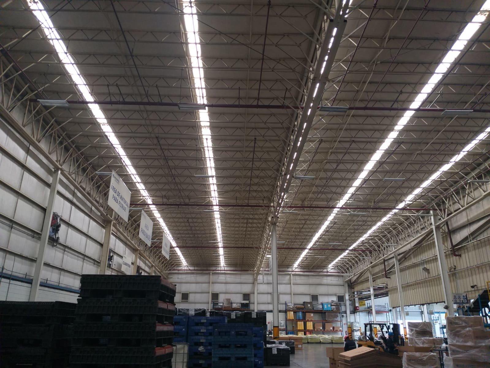 Cubierta de armaduras metálicas de una nave industrial iluminada por luminarias lineales, vista a contrapicado