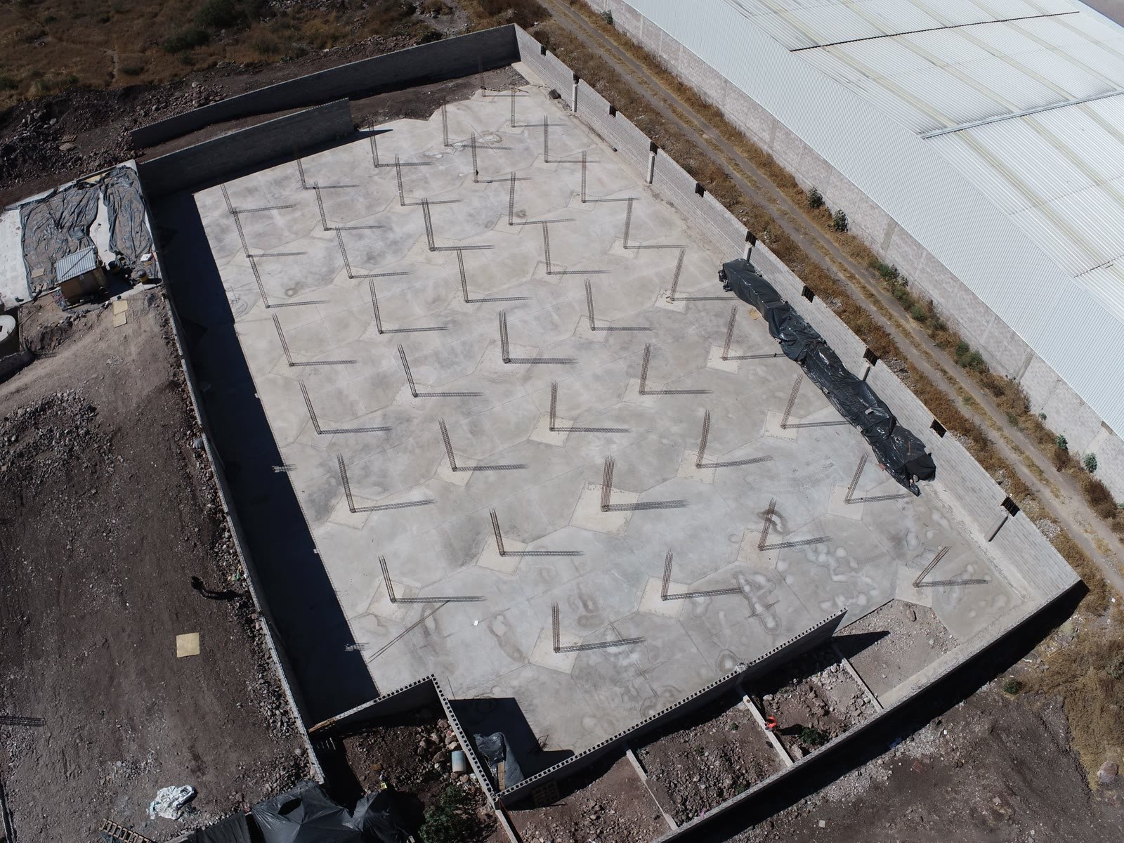 Vista aérea cenital de la losa de cimentación terminada de una nave industrial, con la retícula completa de arranques de columna