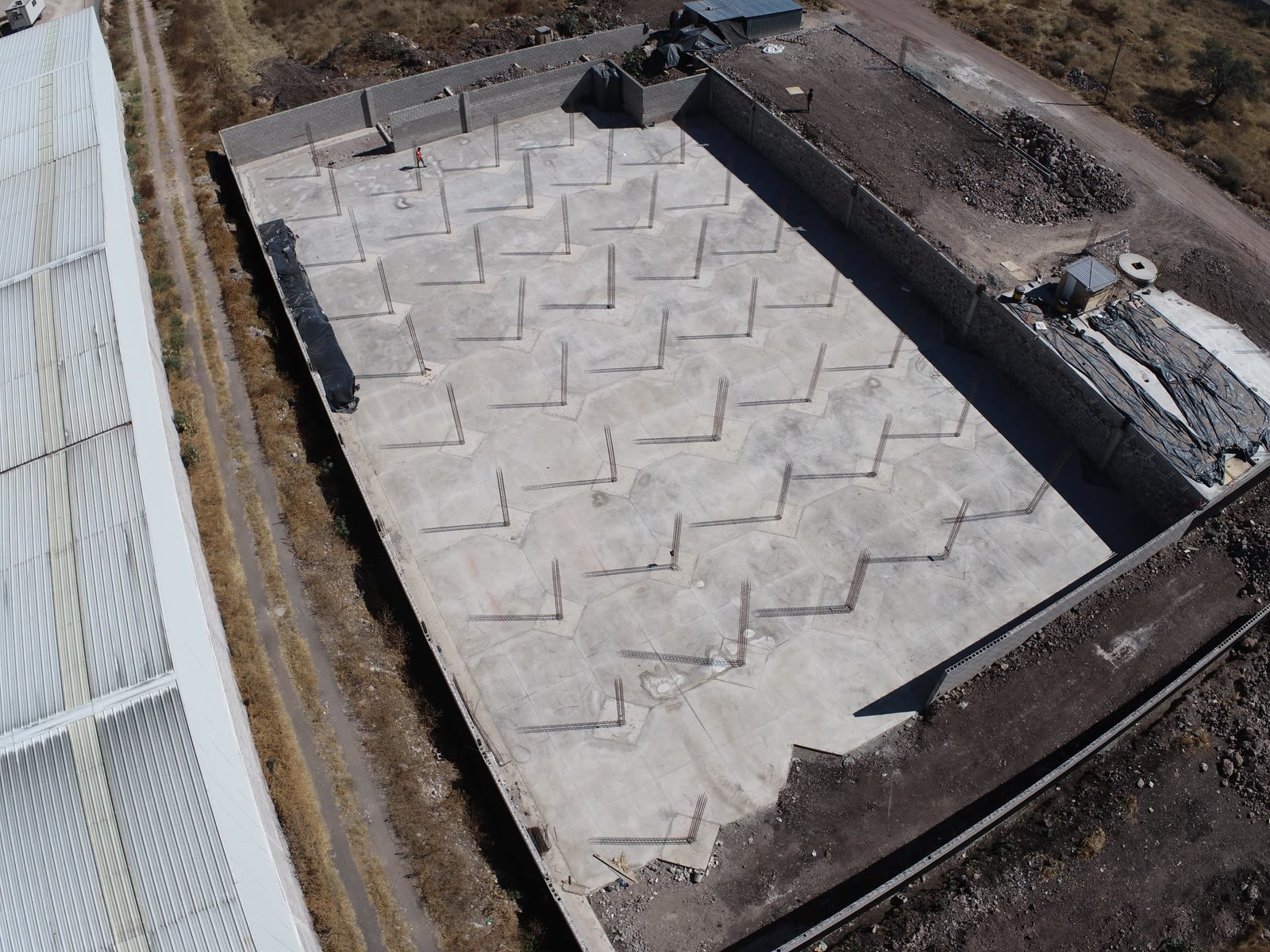 Vista aérea de la nave industrial en obra con la losa colada, los muros perimetrales de block y las preparaciones de columna
