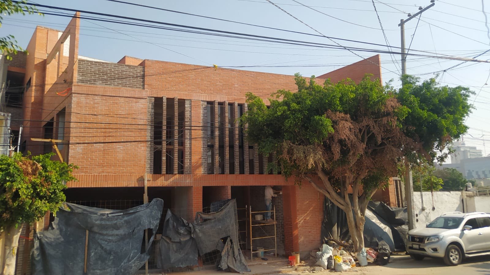 E9 — fachada de tabique aparente con celosía vertical, avance de obra desde la calle