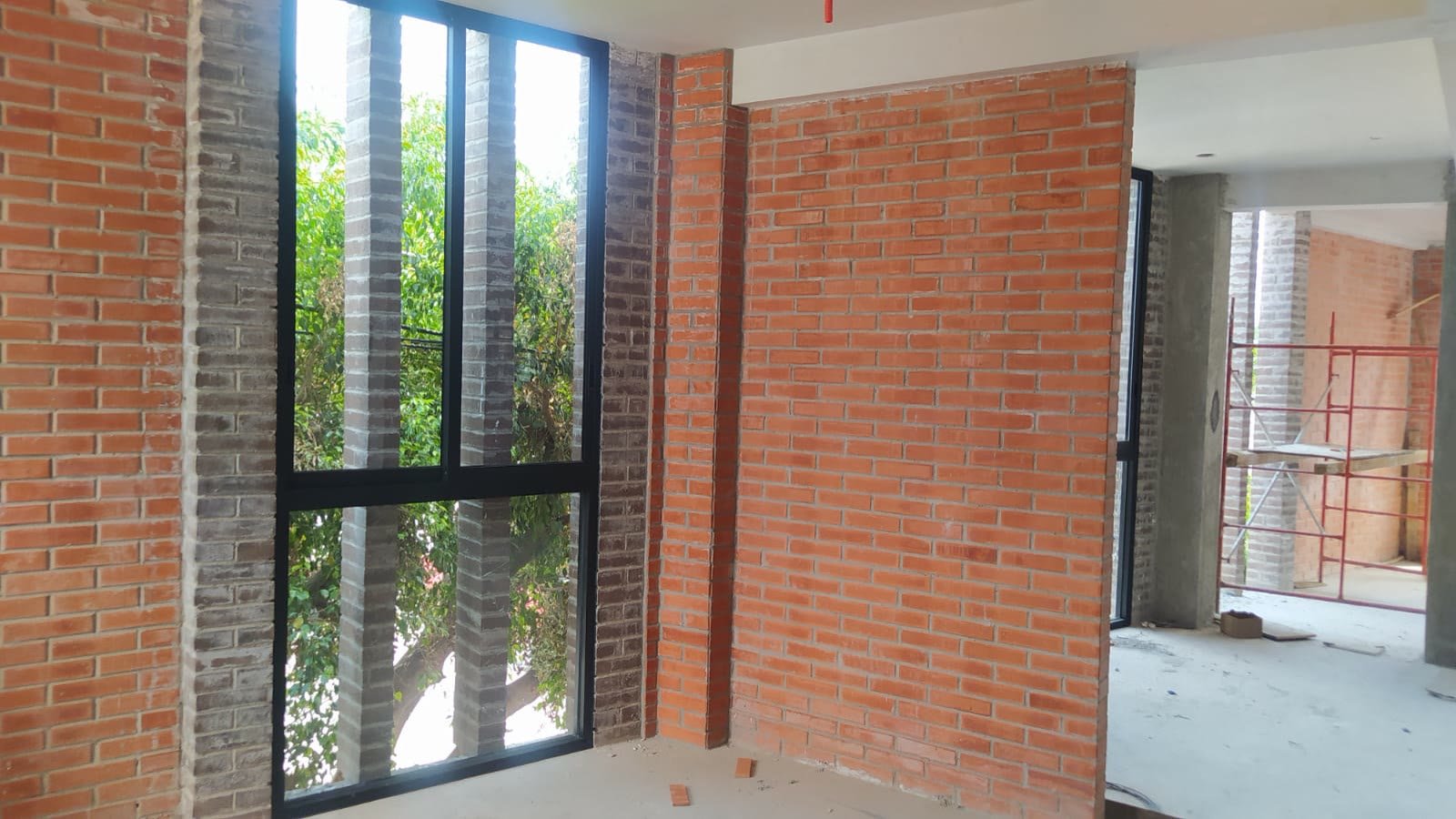E9 — interior de un departamento con muros de tabique aparente y ventanal de piso a techo entre machones