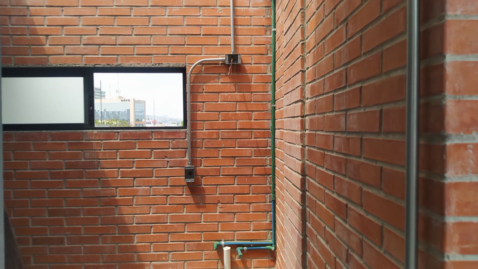 E9 — canalización eléctrica y tubería hidráulica sobre muro de tabique, con vista a la ciudad