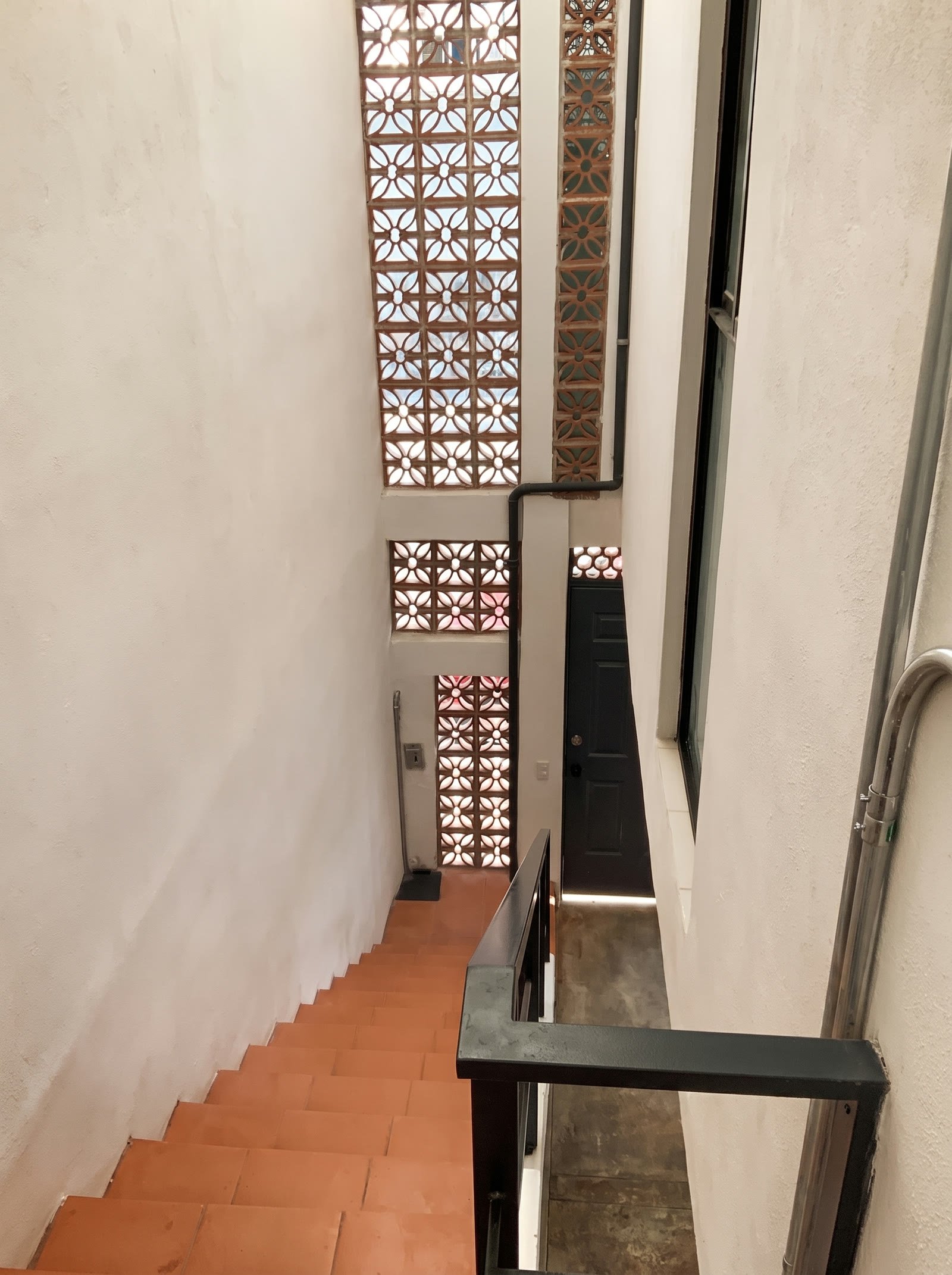 Escalera de barro con barandal de acero junto al cubo de luz con celosía