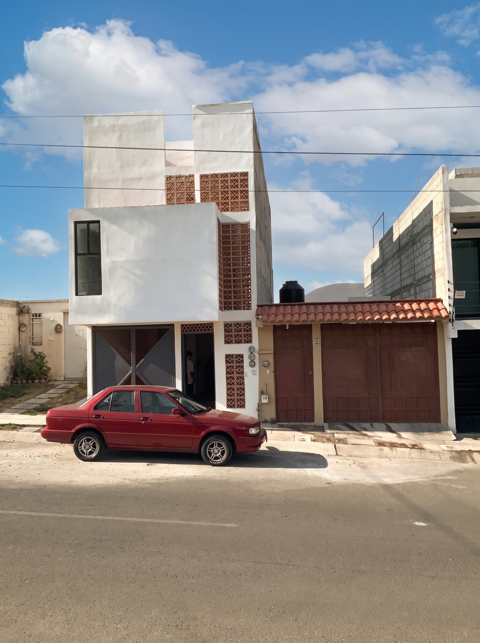 Fachada terminada de la ampliación: volúmenes blancos y franjas de celosía de barro