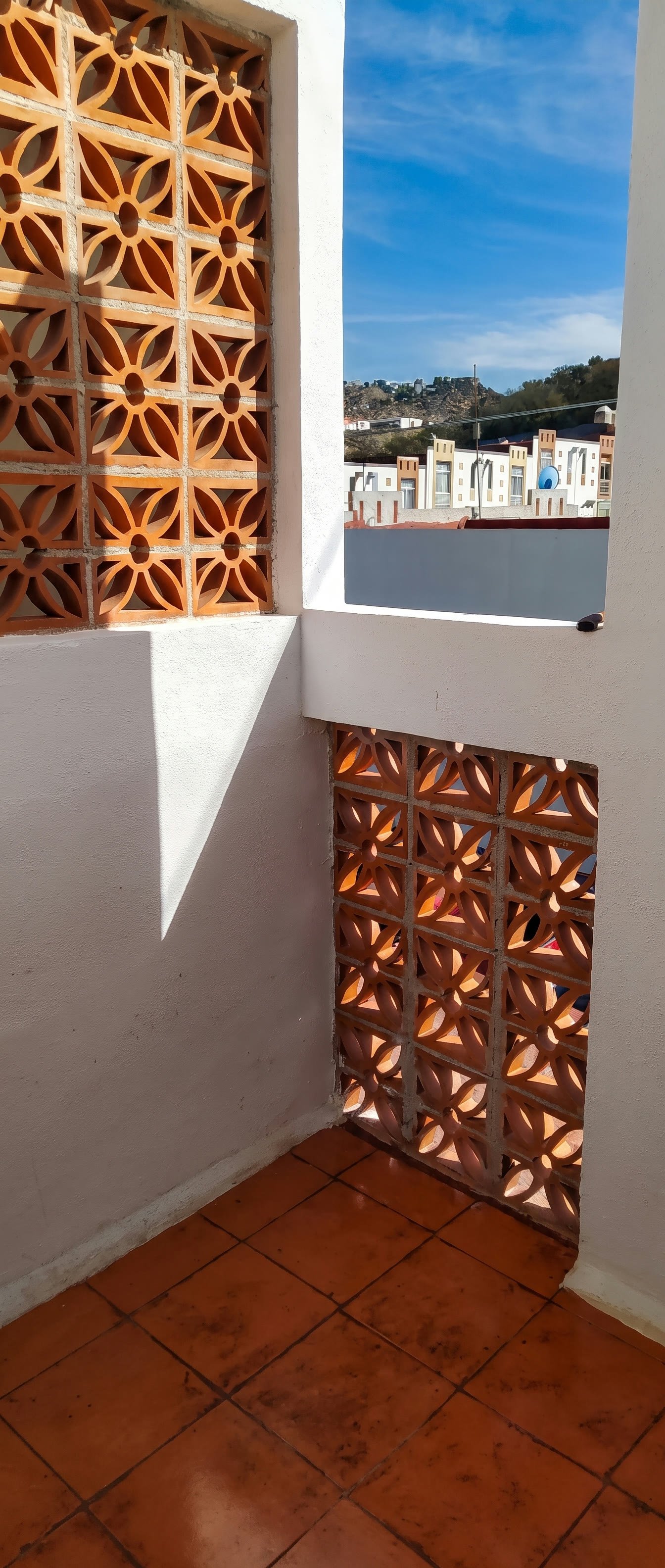 Esquina de la azotea con dos paños de celosía y piso de barro, con la sombra marcada del sol de mediodía