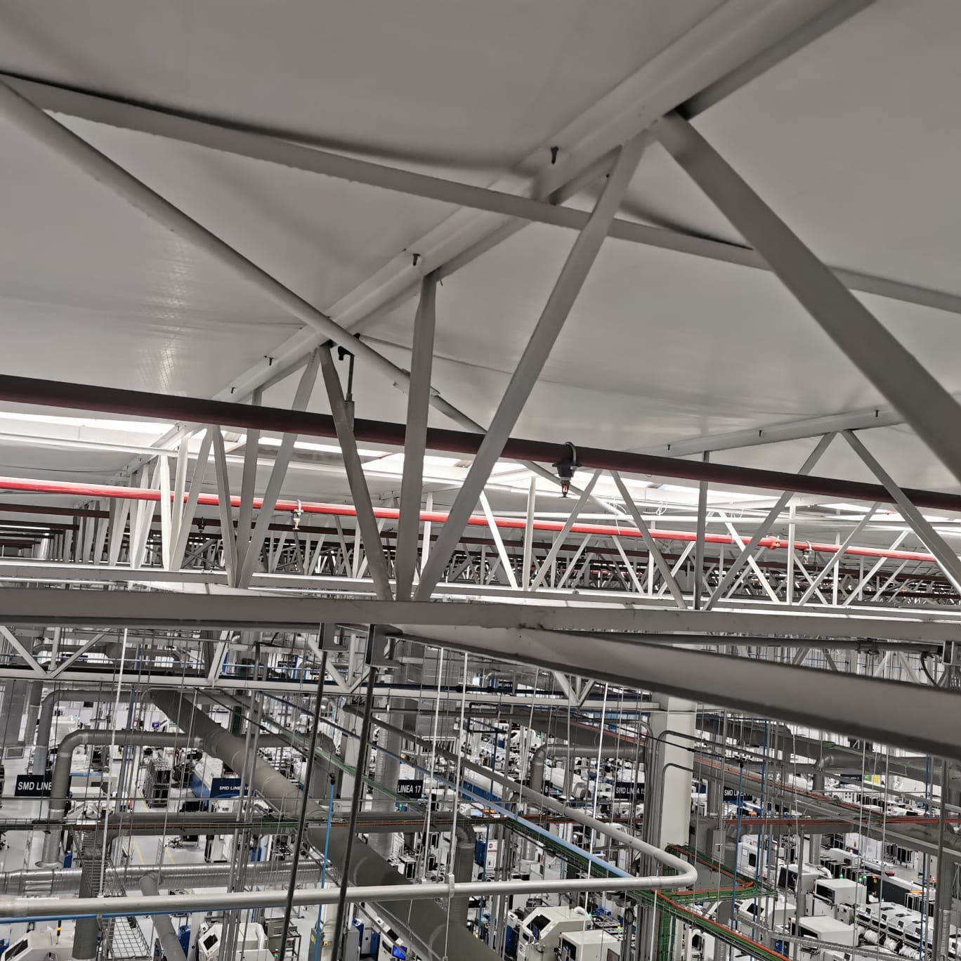 Nave industrial — armaduras metálicas de cubierta con red contra incendios y ductería sobre las líneas de producción