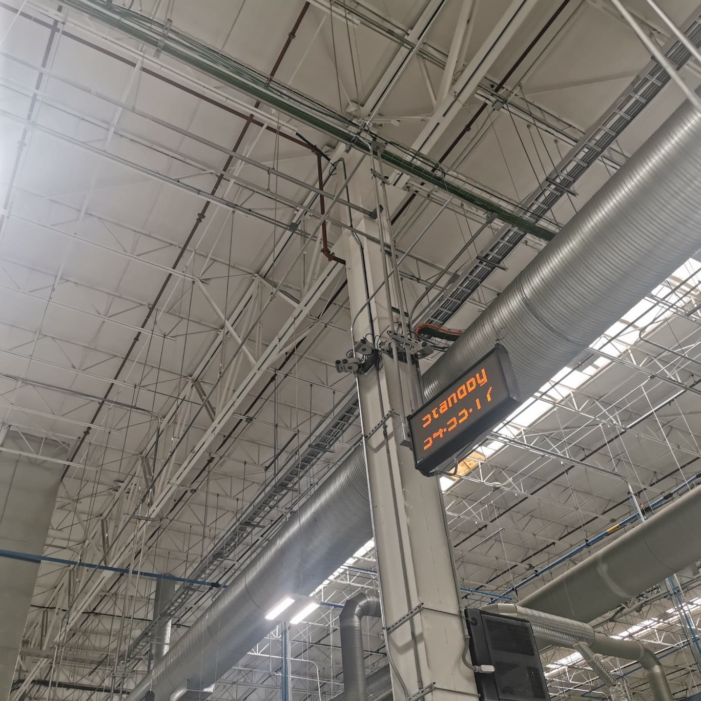 Nave industrial — ductos de aire acondicionado, charolas portacables y rociadores contra incendio bajo la estructura de cubierta