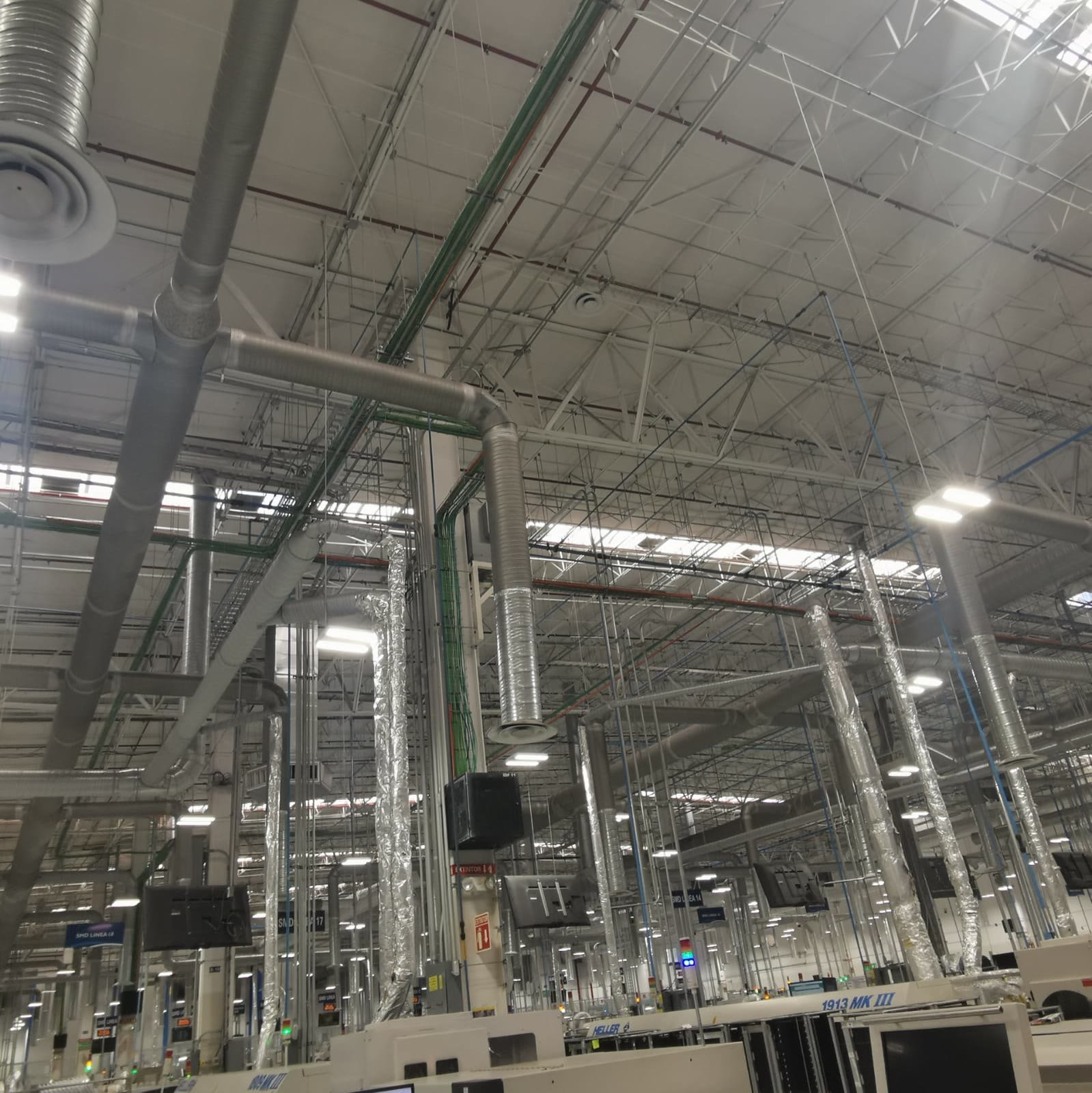 Nave industrial — red de ductería de inyección y extracción con bajantes flexibles hacia las líneas de producción