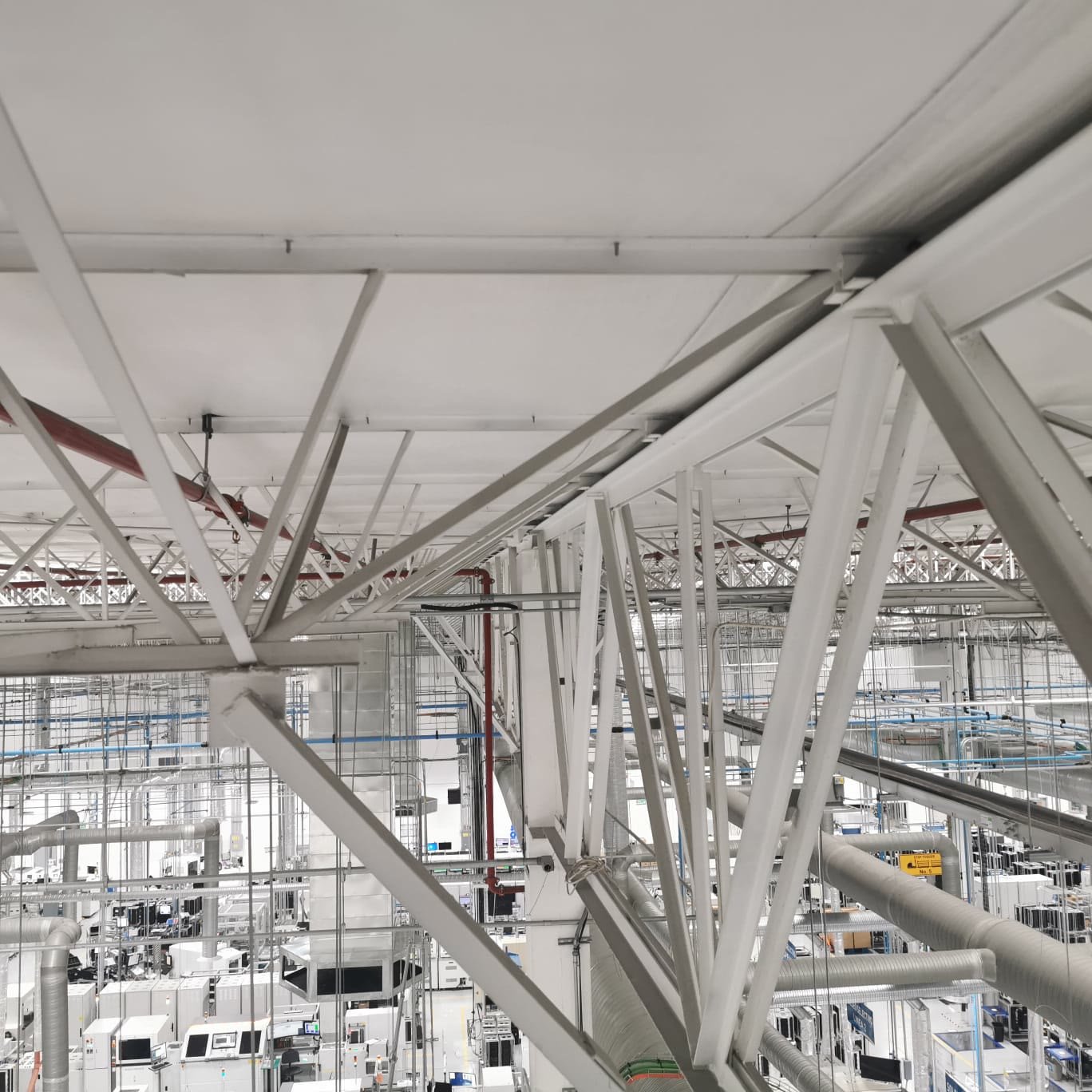 Nave industrial — detalle de la armadura metálica de cubierta con ductería y tubería contra incendios vista desde altura