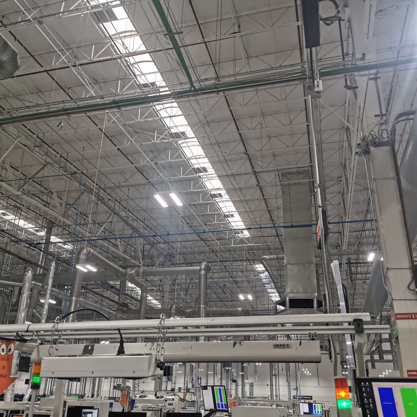 Nave industrial — ductos troncales de aire acondicionado y difusores sobre el área de producción