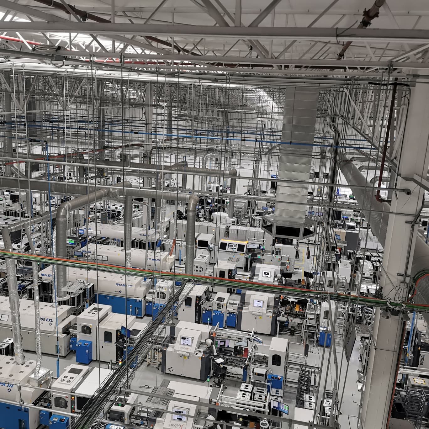 Nave industrial — vista aérea del piso de producción con la ductería de extracción bajando a cada equipo