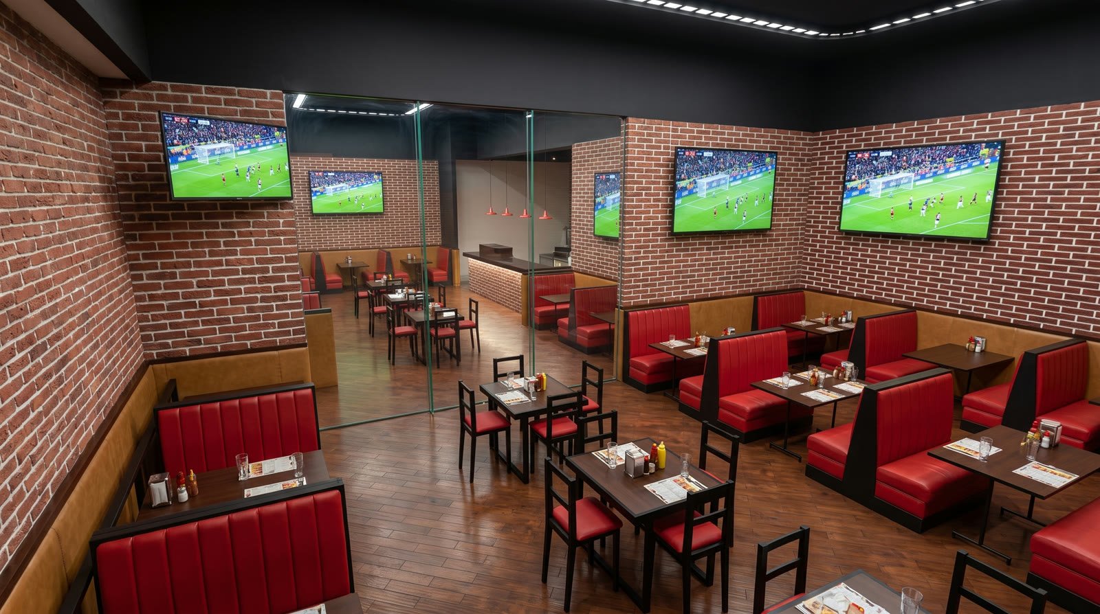 Render del salón principal del restaurante Rebel Wings Coapa: booths tapizados en rojo, muros de ladrillo aparente, piso de duela y pantallas de deportes