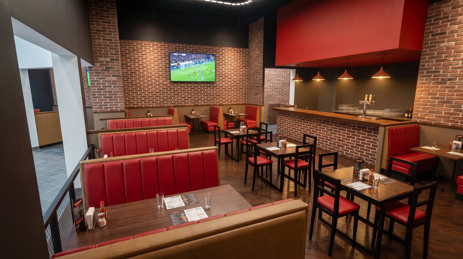 Render del comedor en dos niveles del restaurante, con barra de tiro de cerveza al fondo y booths rojos sobre muro de ladrillo