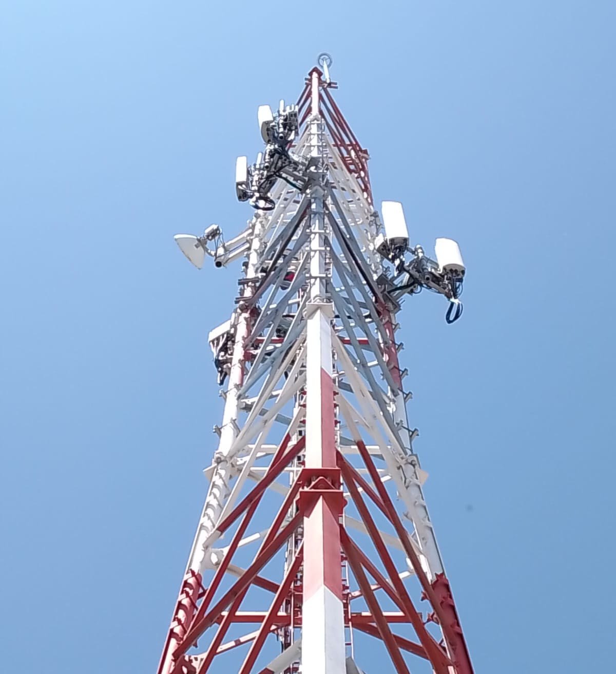 Torre autosoportada de telecomunicaciones en rojo y blanco vista en contrapicado contra el cielo azul, con los montantes de acero galvanizado del refuerzo ya instalados