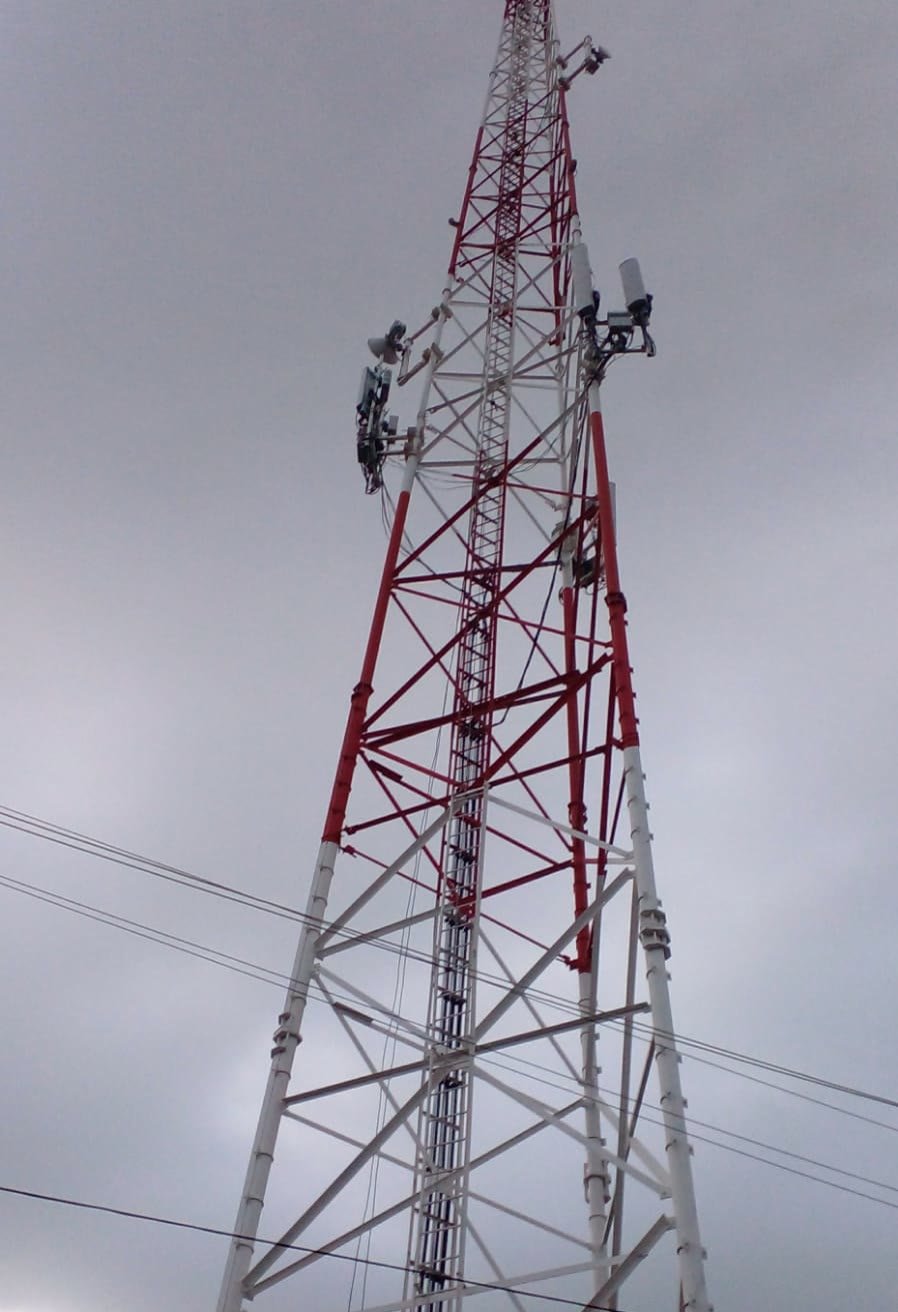 Torre autosoportada de telecomunicaciones en rojo y blanco vista desde su base, con antenas y radios instalados en los niveles superiores