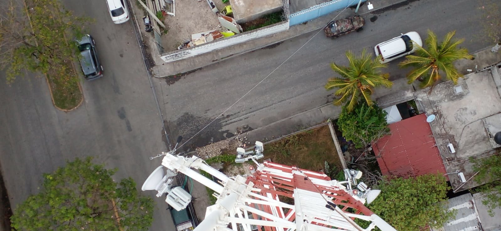 Vista en picada desde la punta de una torre de telecomunicaciones: la celosía metálica desciende sobre la calle y las casas del barrio