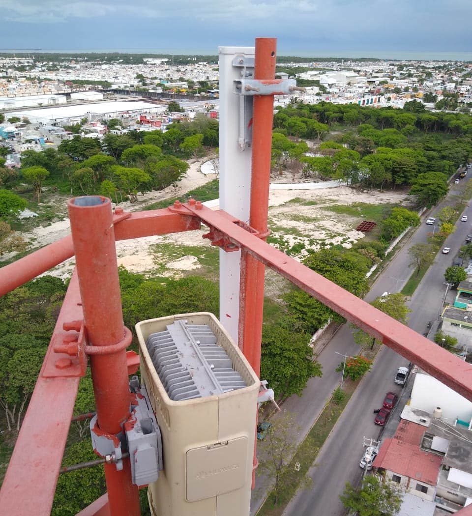Radio de telecomunicaciones montado en la celosía de la torre, con la ciudad costera extendida al fondo