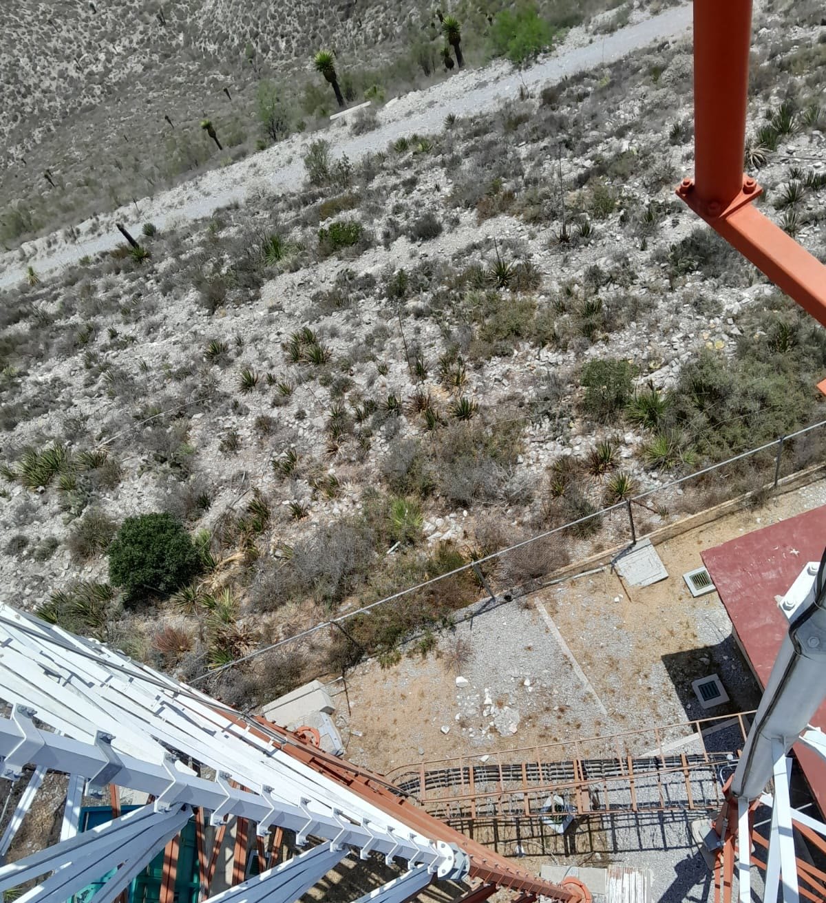 Estructura de acero de una torre autosoportada vista desde altura, con la ladera rocosa y los magueyes del semidesierto neoleonés al fondo